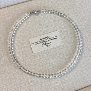 Detailed view of a transparent bead necklace with a silver magnetic clasp on beige linen