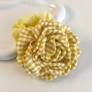 Détail d'un chouchou à carreaux jaunes avec rose en 3D sur un plateau blanc
