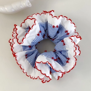 Détail d'un chouchou à carreaux bleus avec bordure volantée blanche et broderie rouge