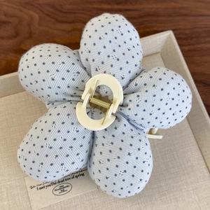 Détail d'une pince à cheveux fleur à pois bleus posée sur un plateau en tissu beige