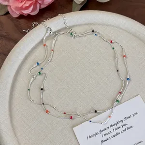 Elegant silver snake chain necklace with colorful enamel beads on a beige ceramic tray