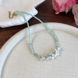 Détail du collier de perles facettées vert clair avec fleurs blanches et fermoir doré