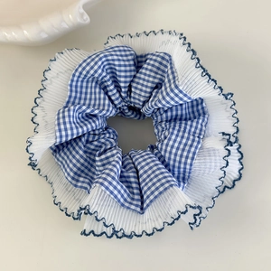 Détail d'un chouchou à carreaux bleus avec bordure en dentelle blanche et festons bleus