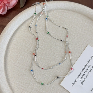 Silver snake chain necklace with colorful enamel beads displayed on a beige tray