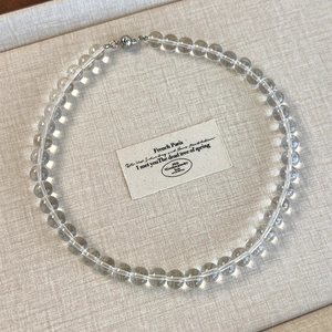 Detailed view of clear acrylic beaded choker with secure magnetic metal closure on a beige board