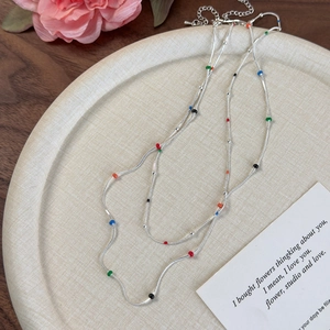 Silver layered snake chain necklace with colorful enamel beads on a decorative plate
