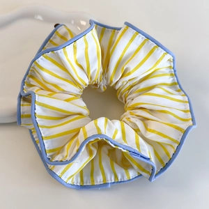Détail d'un chouchou à rayures jaunes et blanches avec bordure bleue sur fond blanc