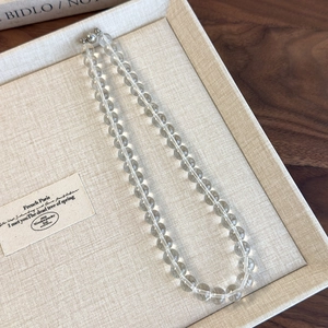 Macro shot of transparent acrylic round bead choker with metallic clasp on beige tray