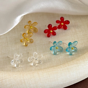 Gros plan de quatre boucles d'oreilles florales colorées en rouge, bleu et ambre sur soie