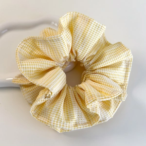 Détail d'un chouchou à carreaux jaunes avec plis en tissu doux sur un plateau blanc pur