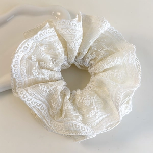 Détail d'un chouchou en dentelle blanche avec broderies florales sur tissu en maille douce