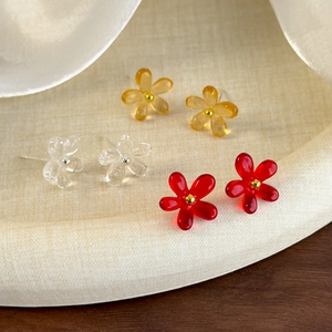 Vue macro de boucles d'oreilles fleurs transparentes, ambre et rouges sur plateau en tissu