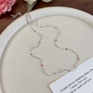 Detail of silver snake chain necklace with colorful enamel beads on a beige tray
