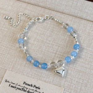 Détail du bracelet en perles de verre bleu clair avec breloque coeur sur tissu beige