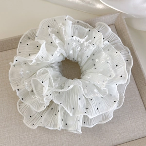 Detailed view of a white lace scrunchie with black polka dots and floral embroidery