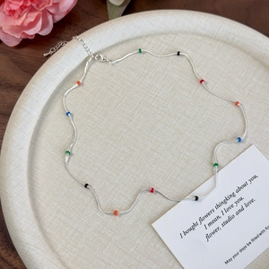 Detail of silver snake chain necklace with colorful enamel beads on a beige tray