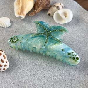 Détail d'une pince à cheveux étoile de mer avec texture marbrée bleue et strass verts