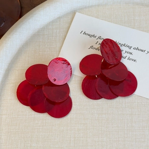 Détail de boucles d'oreilles pompons en nacre rouge posées sur un plateau blanc