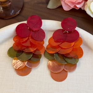 Détail de disques en résine colorés sur de longues boucles d'oreilles pompons sur un plateau