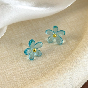 Gros plan de boucles d'oreilles fleurs bleues translucides avec un centre doré sur tissu