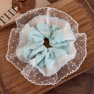 Close-up detail of mint green lace scrunchie with white polka dots on wood tray