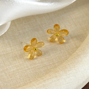 Vue macro de boucles d'oreilles fleurs ambrées translucides avec perle dorée et résine