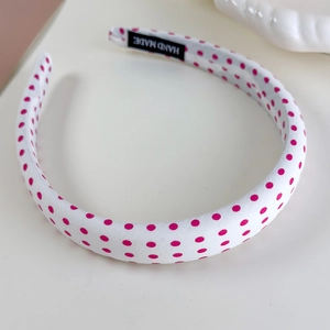 Detail of white headband with pink polka dots featuring a black Hand Made woven label