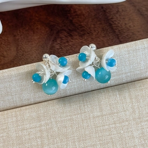 Detailed close-up of mint green floral stud earrings with white petals and blue beads
