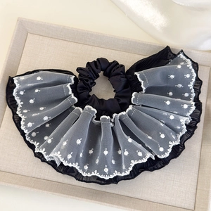 Detail of black scrunchie with white lace polka dot edges on a textured tray