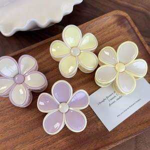 Détail de pinces à cheveux en forme de fleurs jaune crème et lilas sur plateau en bois