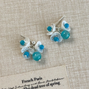 Detailed view of floral stud earrings with white petals and blue beads on a linen background