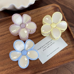 Détail de trois pinces à cheveux fleurs crème en rose, jaune et bleu sur un plateau bois