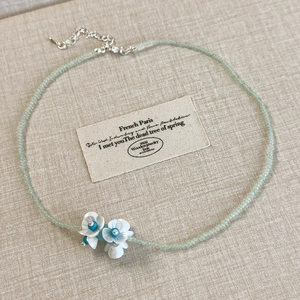 Detail of mint green beaded necklace with white lily of the valley flower pendants