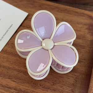 Détail d'une pince à cheveux fleurie crème et violette sur un plateau en bois