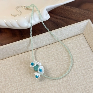 Detail of mint green beaded necklace featuring delicate white lily flowers and silver chain