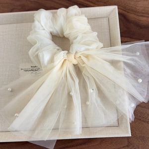 Détail d'un chouchou en maille blanc crème avec de longs rubans élégants et des perles