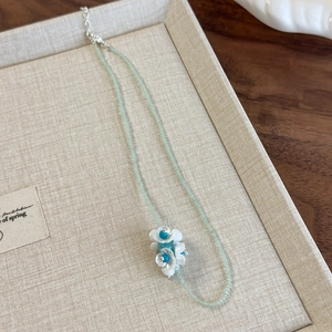 Detail of mint green beaded necklace with white flower pendant on a beige texture display