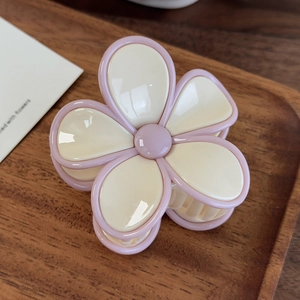 Détail d'une pince à cheveux fleurie crème et rose sur un plateau en bois noir