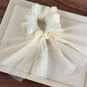 Détail du chouchou en organza blanc cassé avec volants et rubans élégants ornés de perles