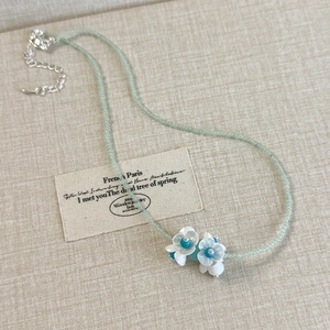Detail of mint green bead necklace with three white resin flowers and blue centers