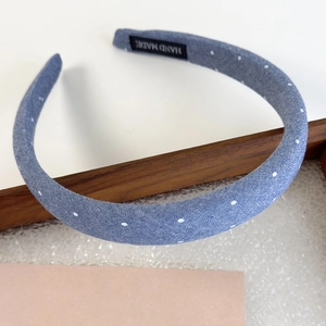 Detail of light blue polka dot denim headband featuring a black woven Handmade label