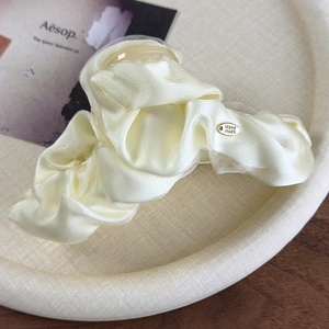 Detail of cream pleated fabric hair claw clip with golden Hand Made metal logo