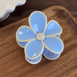 Vue détaillée d'une pince à cheveux fleur bleue avec des accents crème doux