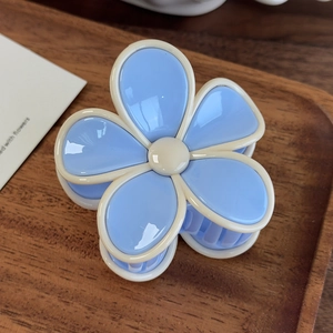 Détail d'une pince à cheveux en forme de fleur bleu clair et crème sur un plateau