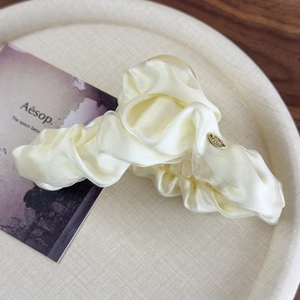 Detailed close-up of cream satin hair scrunchie with elegant folds and gold oval pendant