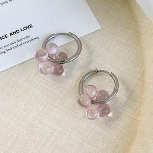 Detail of silver hoop earrings with pink translucent cluster beads on a minimal background