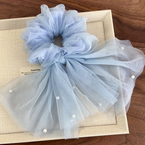 Détail d'un chouchou en résille bleu clair avec perles blanches sur un plateau