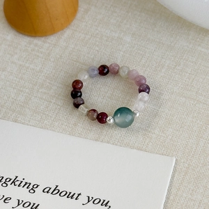 Macro shot of colorful beaded gemstone ring with a green center bead on beige fabric