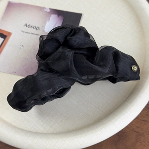 Detail of elegant black mesh hair claw clip with pleated texture on a premium tray