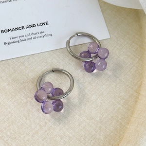 Detailed macro view of purple bead flower charms on silver hoop earrings over textured fabric
